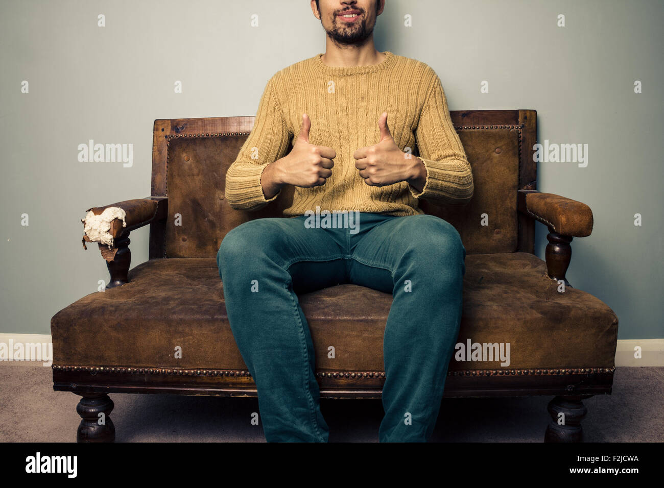 Young man giving thumbs up on sofa Stock Photo