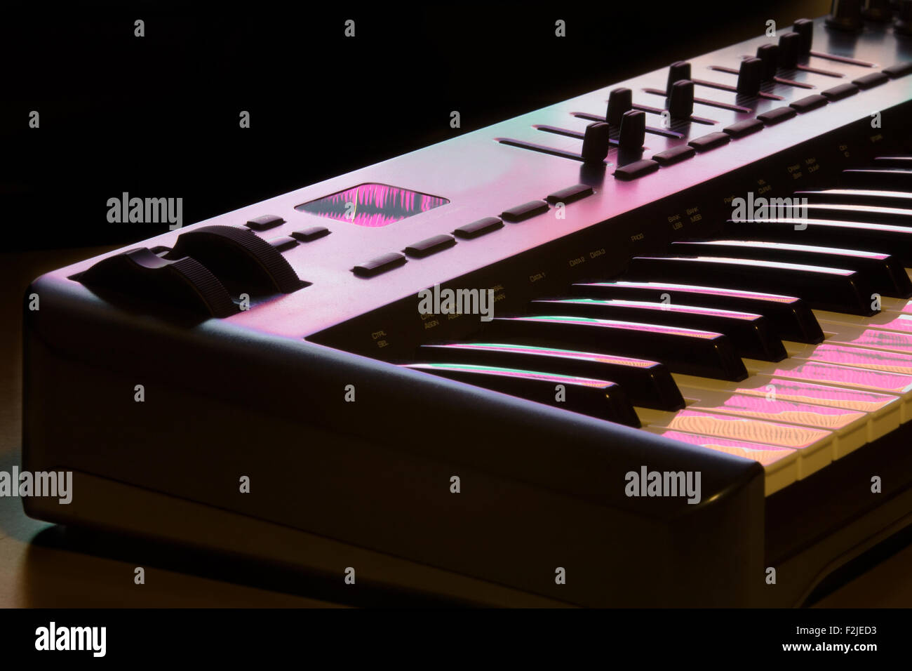 Deatil of a midi keyboard with modulation wheel, lit by a computer