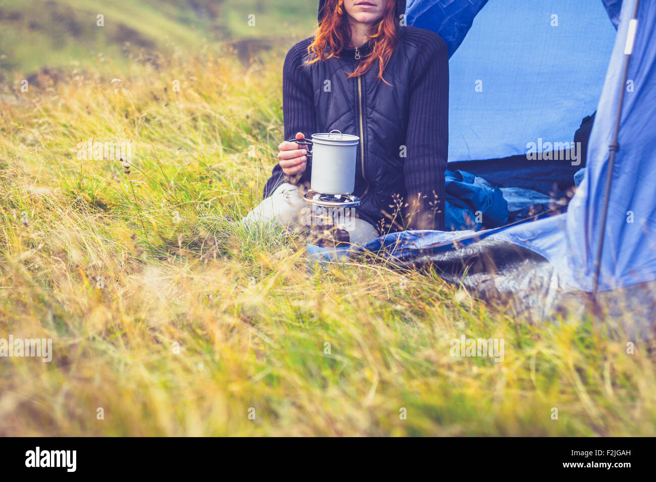 Young woman in tent cooking with portable stove Stock Photo