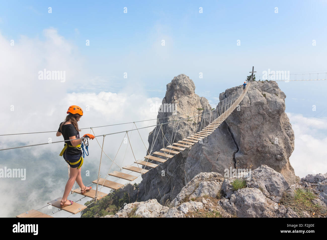 Young woman crossing the chasm on the rope bridge Stock Photo