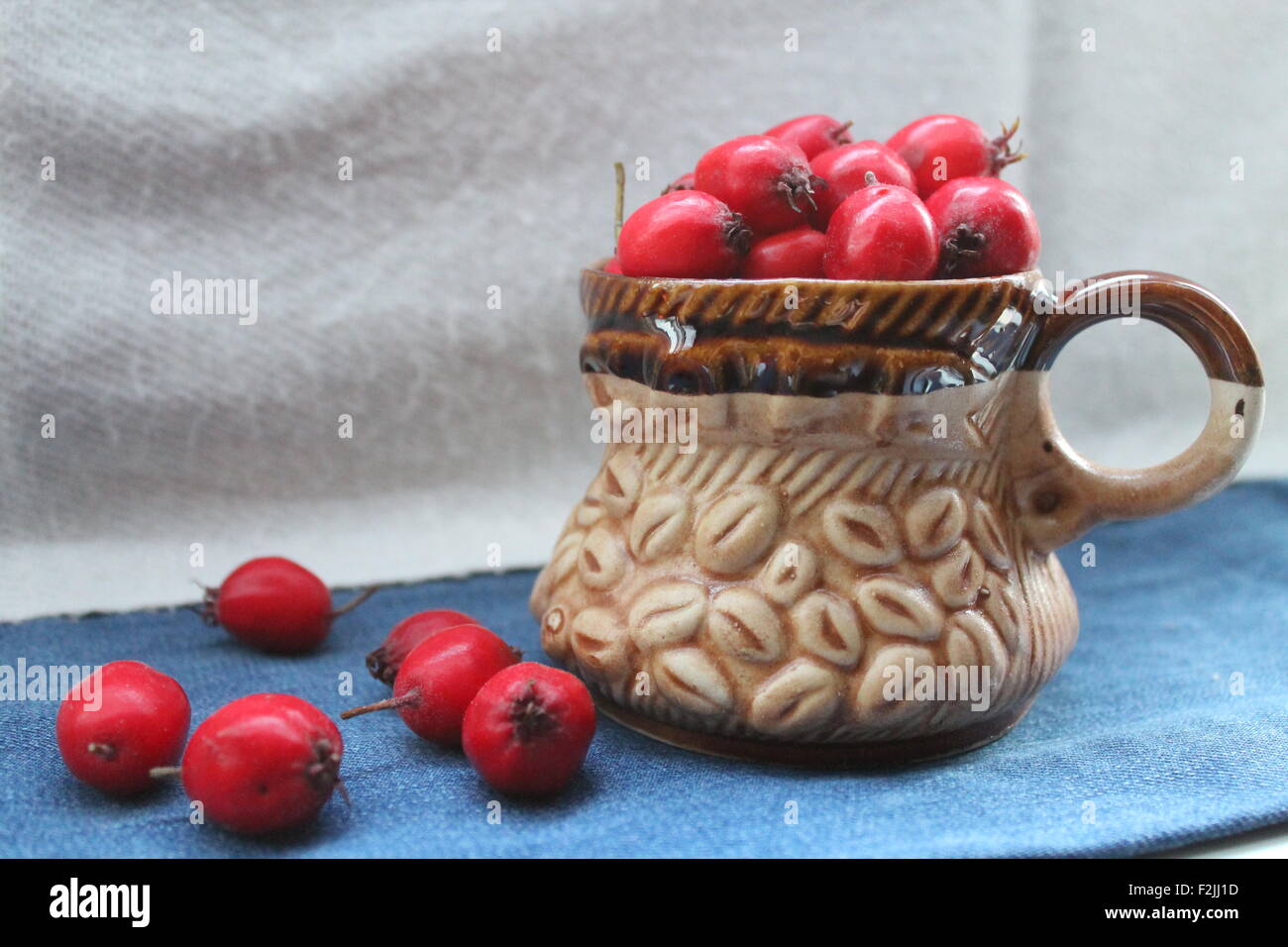 red ripe juicy hawthorn berries in clay brown cup Stock Photo
