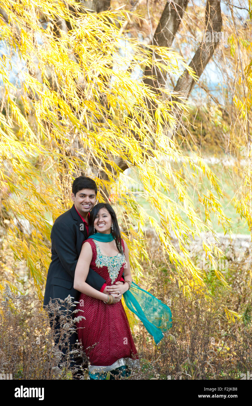 A young and happy Indian couple posing together under a willow tree in ...