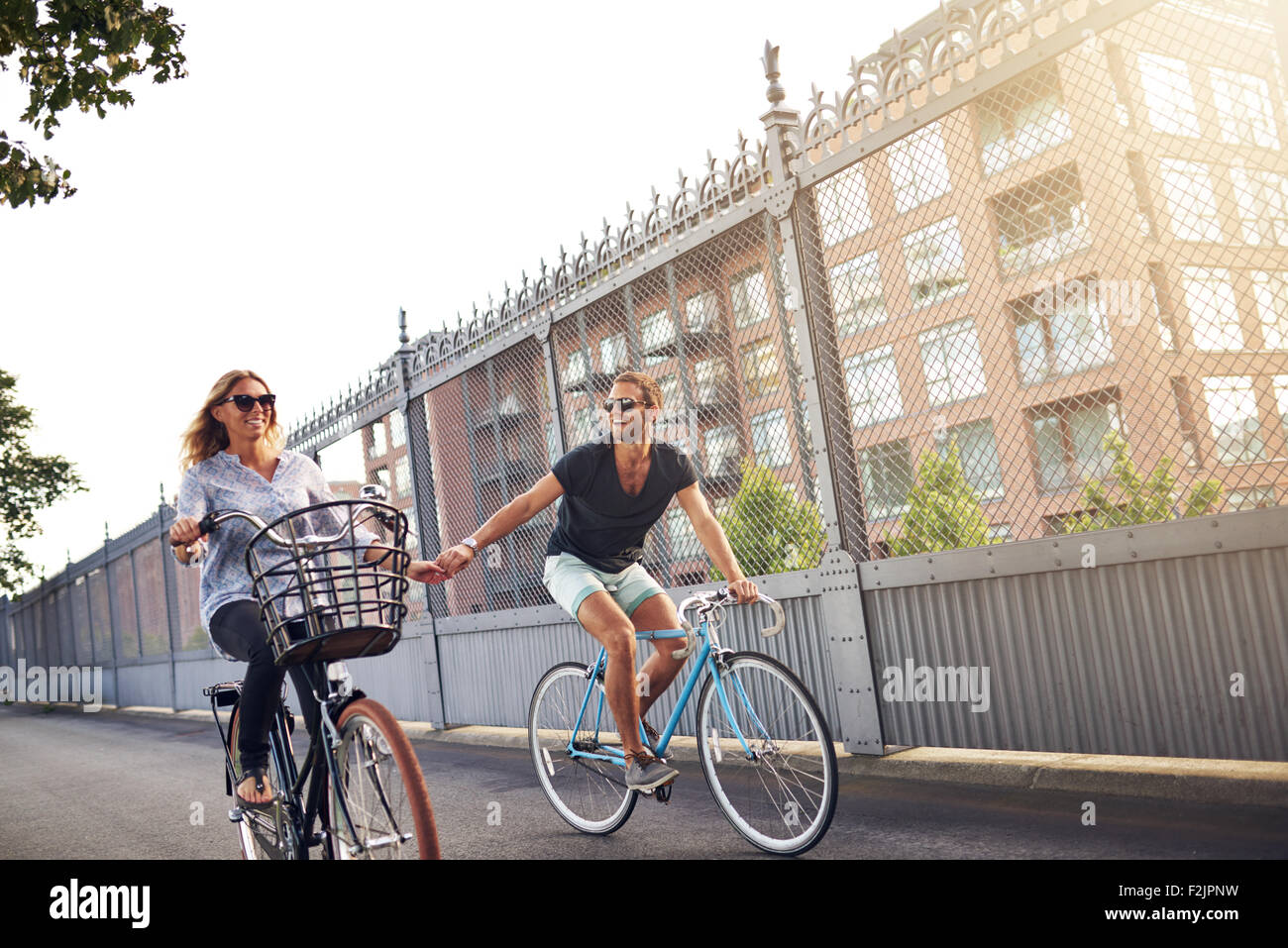 Romantic couple holding hands as they go cycling riding their bikes down an urban street past apartment blocks Stock Photo