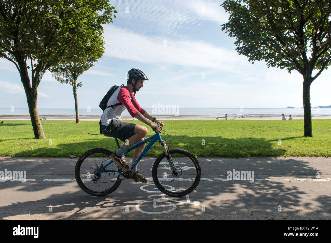 Cyclists cycle in a cycle lane along the Swansea beach promenade in Swansea, South Wales. Stock Photo