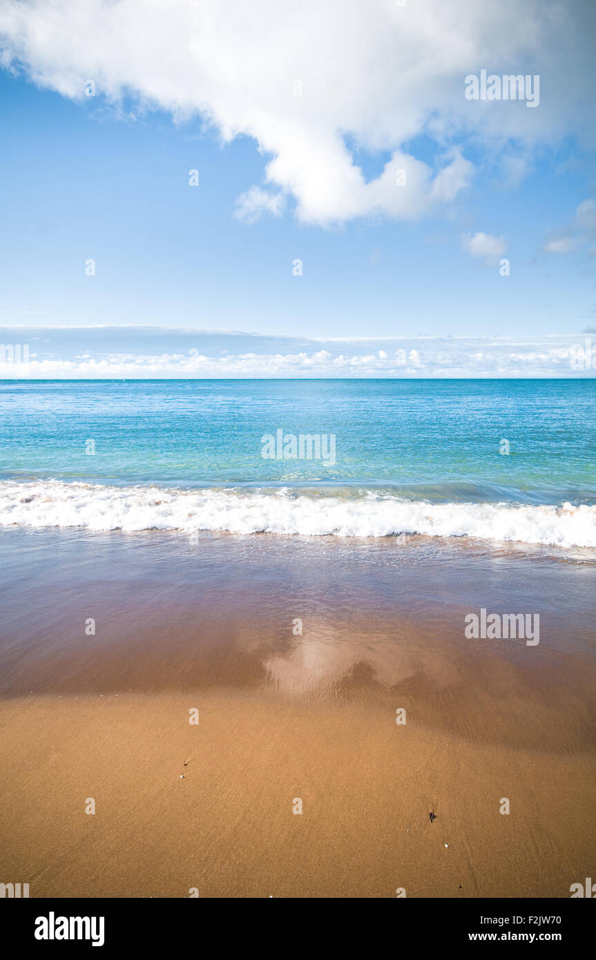 A coastal beach scene with blue sky, sea and golden sand. Stock Photo