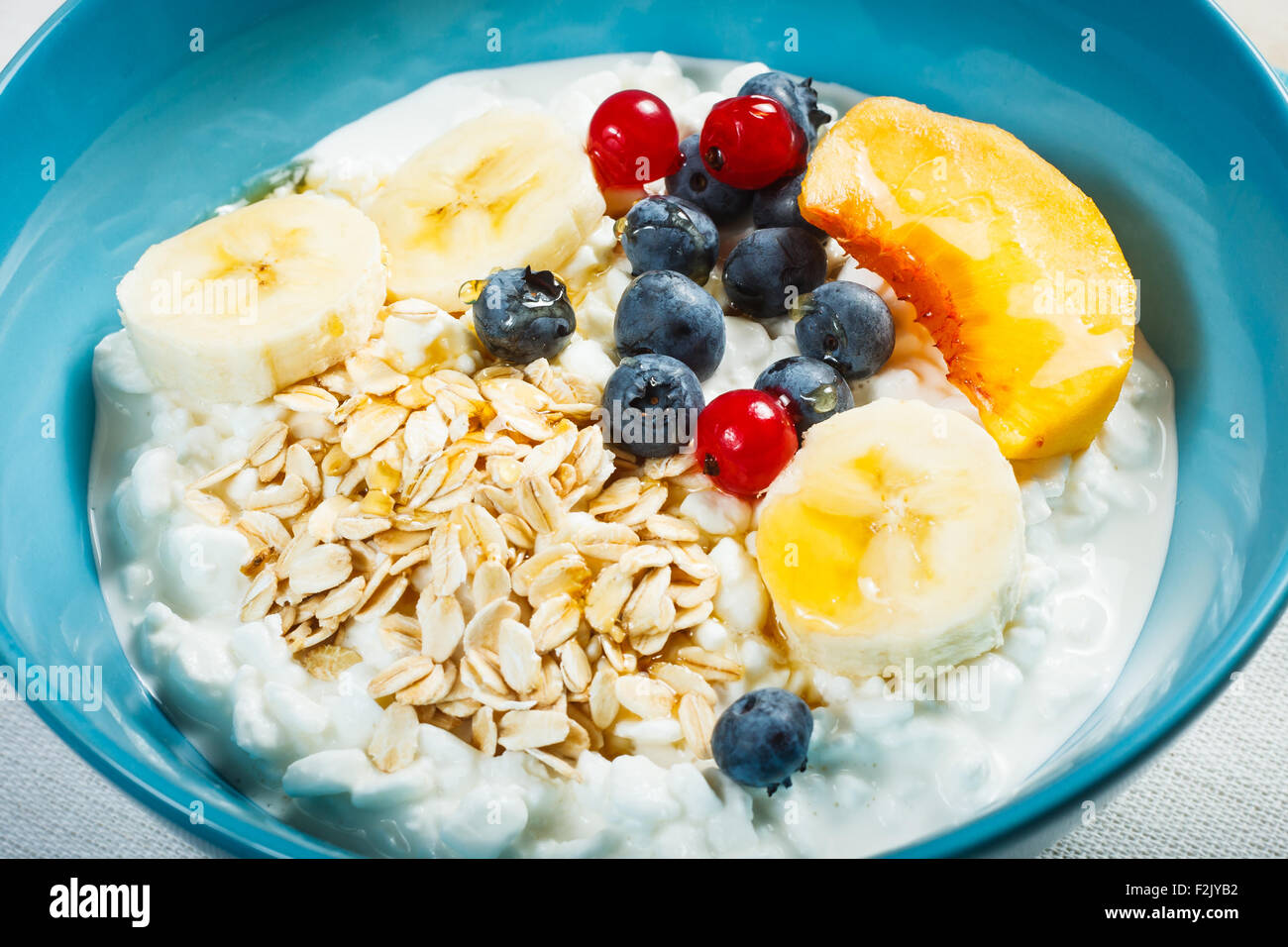 Healthy breakfast. Granulated cottage cheese plus oat flakes, banana, blueberries, red currant, peach and honey. Stock Photo