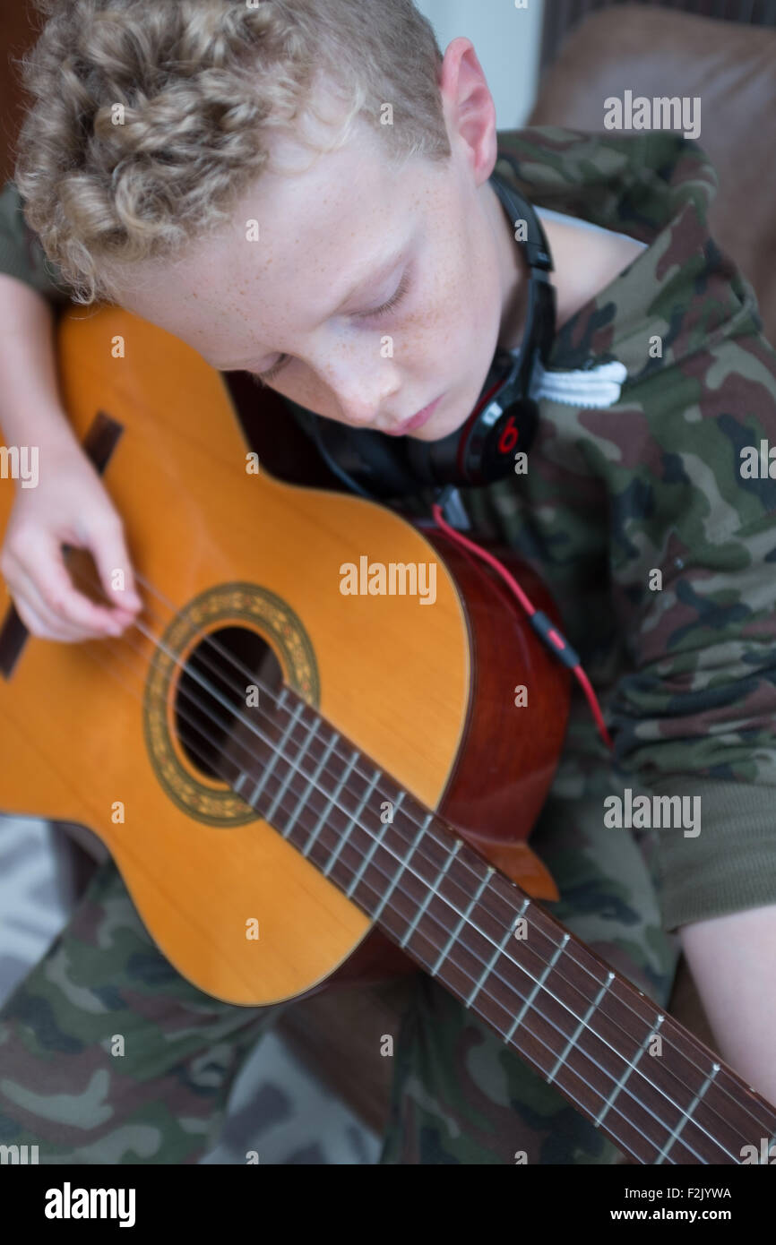 Young blonde caucasian boy 11 years old practising the accoustic guitar wearing beats headphones Stock Photo