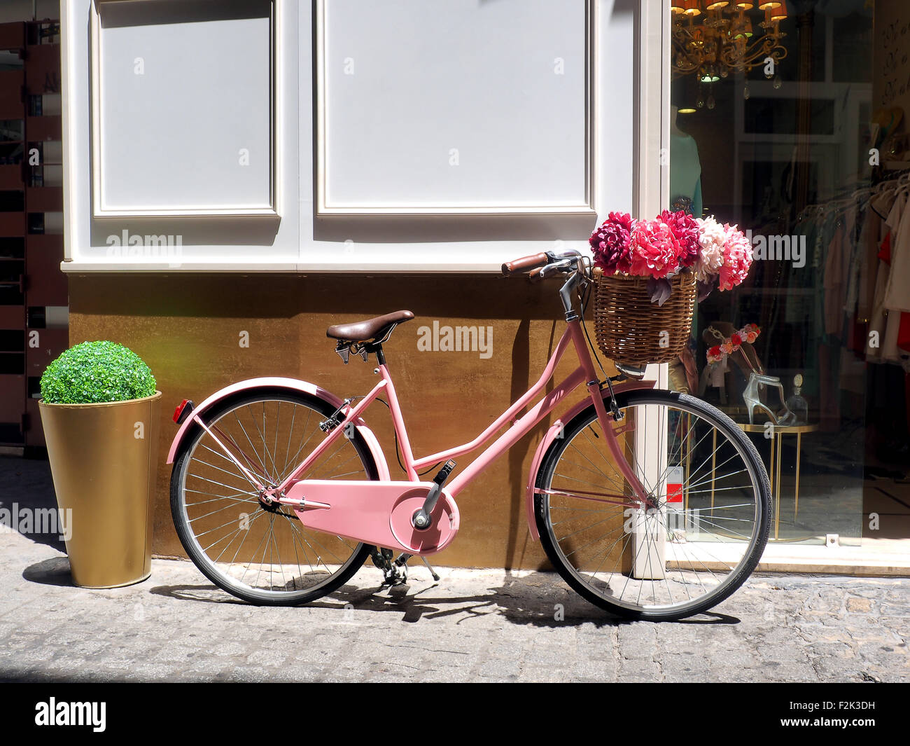 This vintage pink girls bicycle has beautiful pink flowers in a basket on the front of the bike Stock Photo