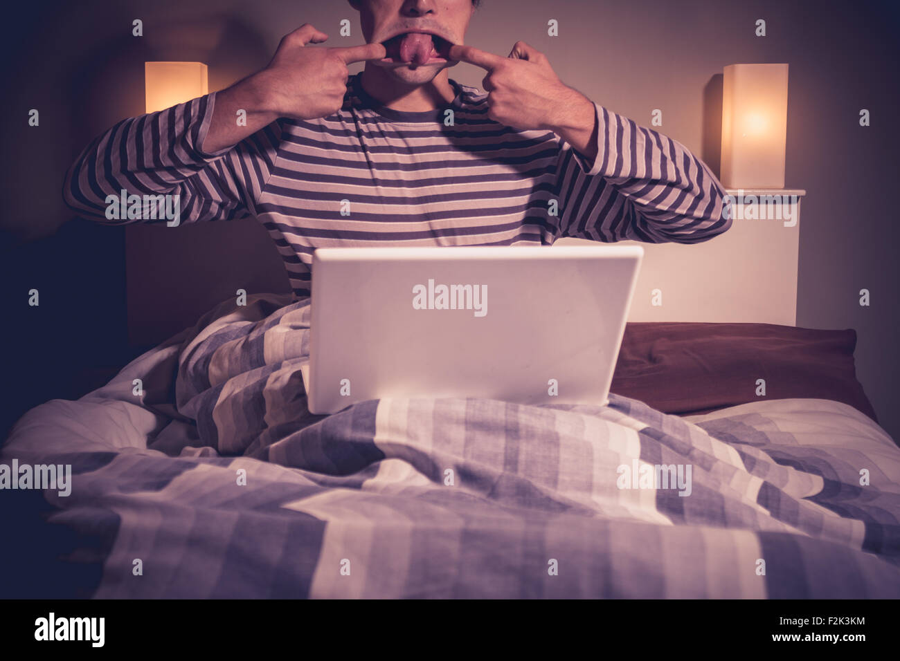 Man pulling faces at laptop in bed at night Stock Photo