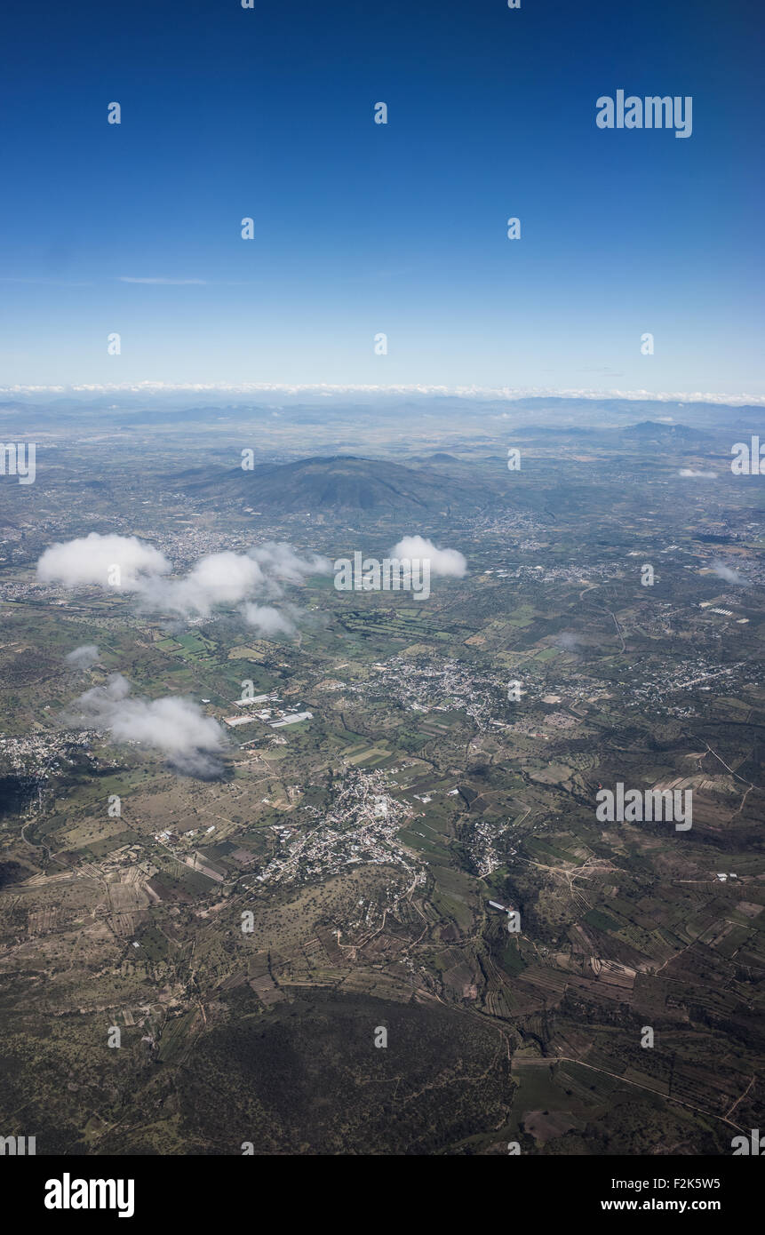Mexico Aerial View Landscape // An aerial view of Mexico unfolds beneath the plane, revealing a diverse tapestry of landscapes. From rugged mountain ranges and sprawling deserts to lush forests and winding coastlines, this bird's-eye perspective showcases the country's rich geographical variety. Cities and rural areas alike punctuate the terrain, offering a stunning visual representation of Mexico's natural beauty and human development. Stock Photo