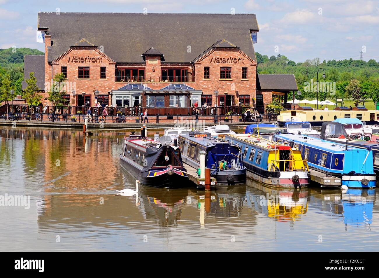 Narrowboats on their moorings in the canal basin with shops, bars and restaurants to the rear, Barton-under-Needwood. Stock Photo