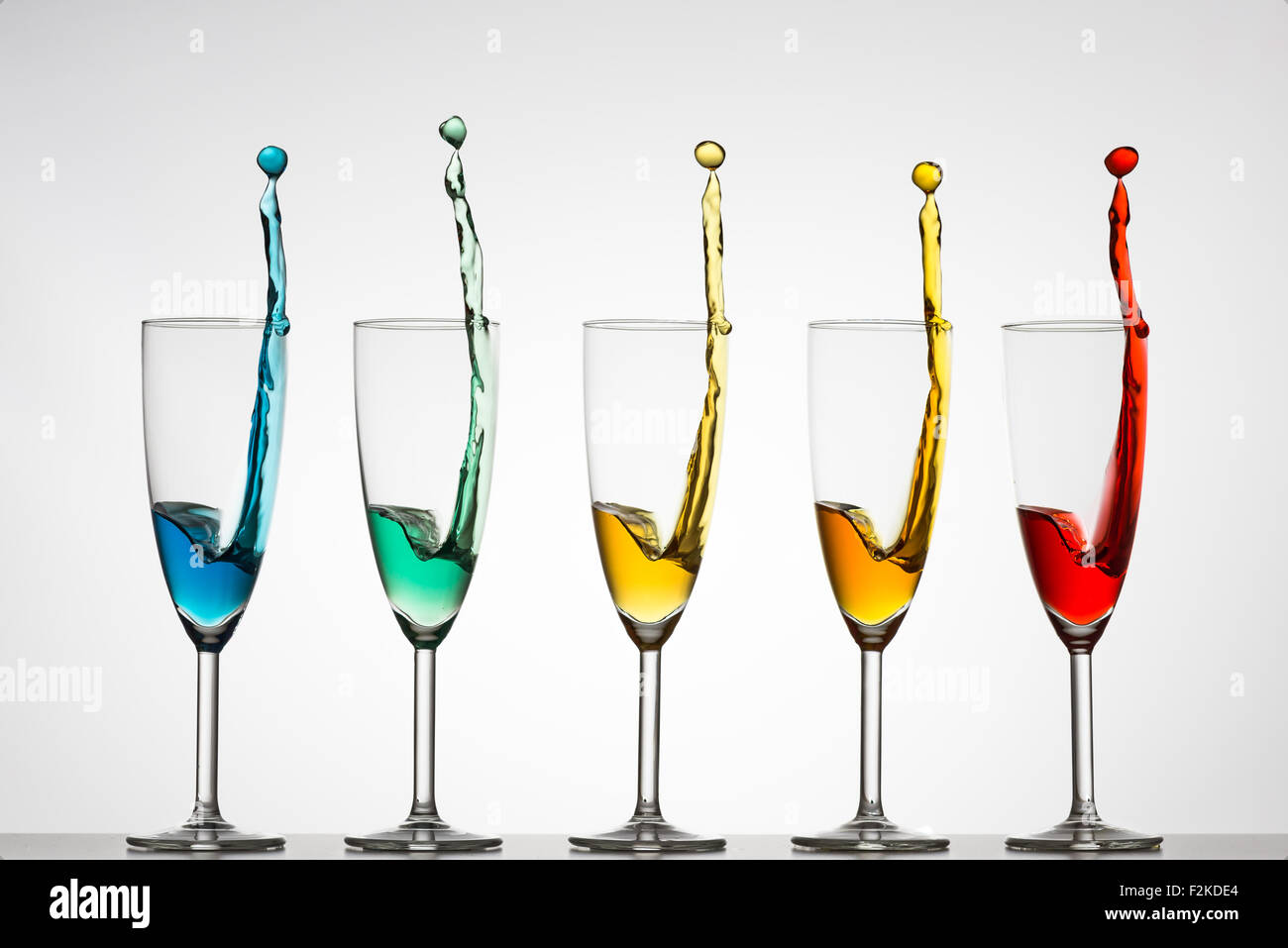 Five champagne flutes with rainbow colored liquid splashing out. High
