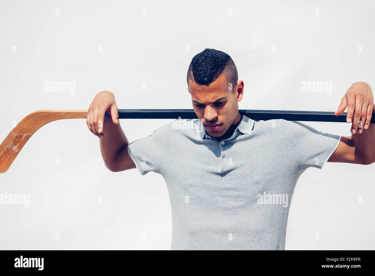 Young man with shaved hair holding hockey stick on his shoulders in