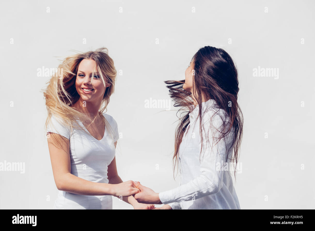 Two young women wearing white clothes tossing her hair in front of white background Stock Photo