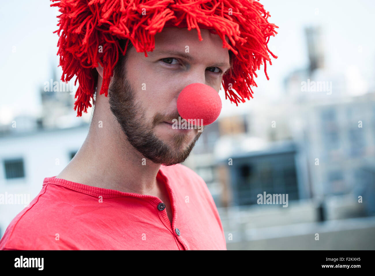 Germany, Cologne, portrait of bearded young man wearing clown's nose and red wig Stock Photo