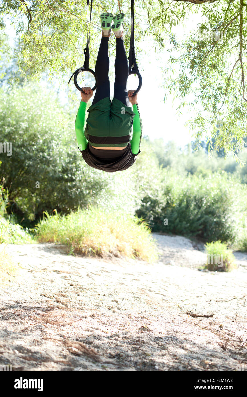 Man doing CrossFit exercises on rings hanging on tree trunk Stock Photo