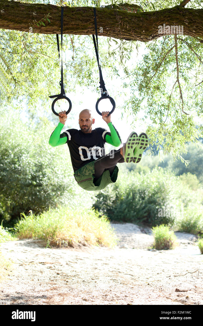 Man doing CrossFit exercise on rings hanging on tree trunk Stock Photo ...