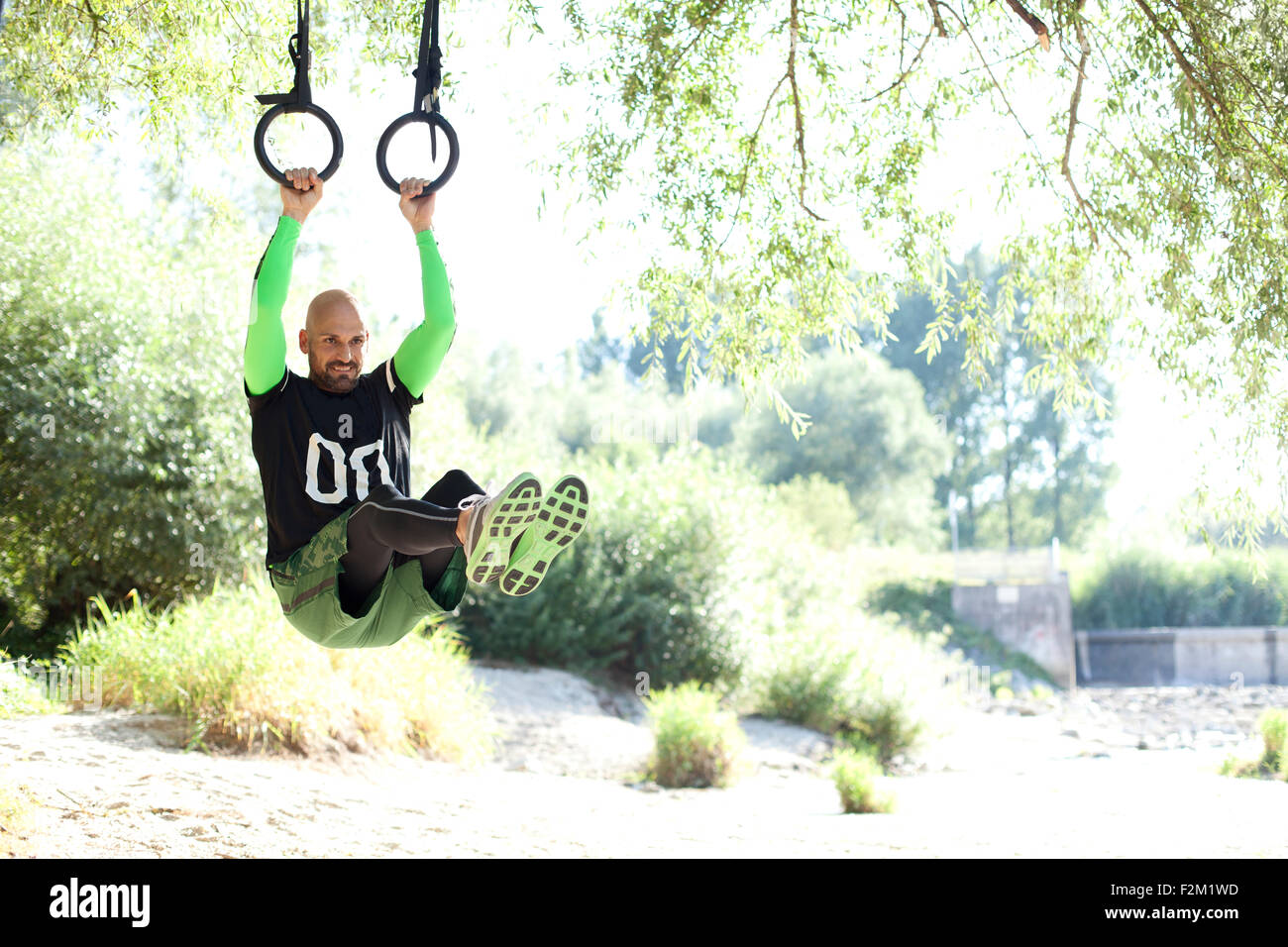 Man doing CrossFit exercise on rings hanging on tree trunk Stock Photo ...