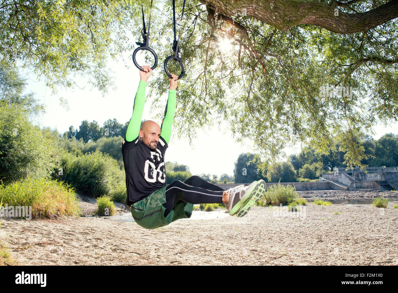 Man doing CrossFit exercise on rings hanging on tree trunk Stock Photo ...