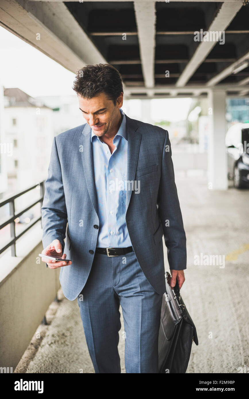 Businessman with briefcase looking at his smartphone Stock Photo