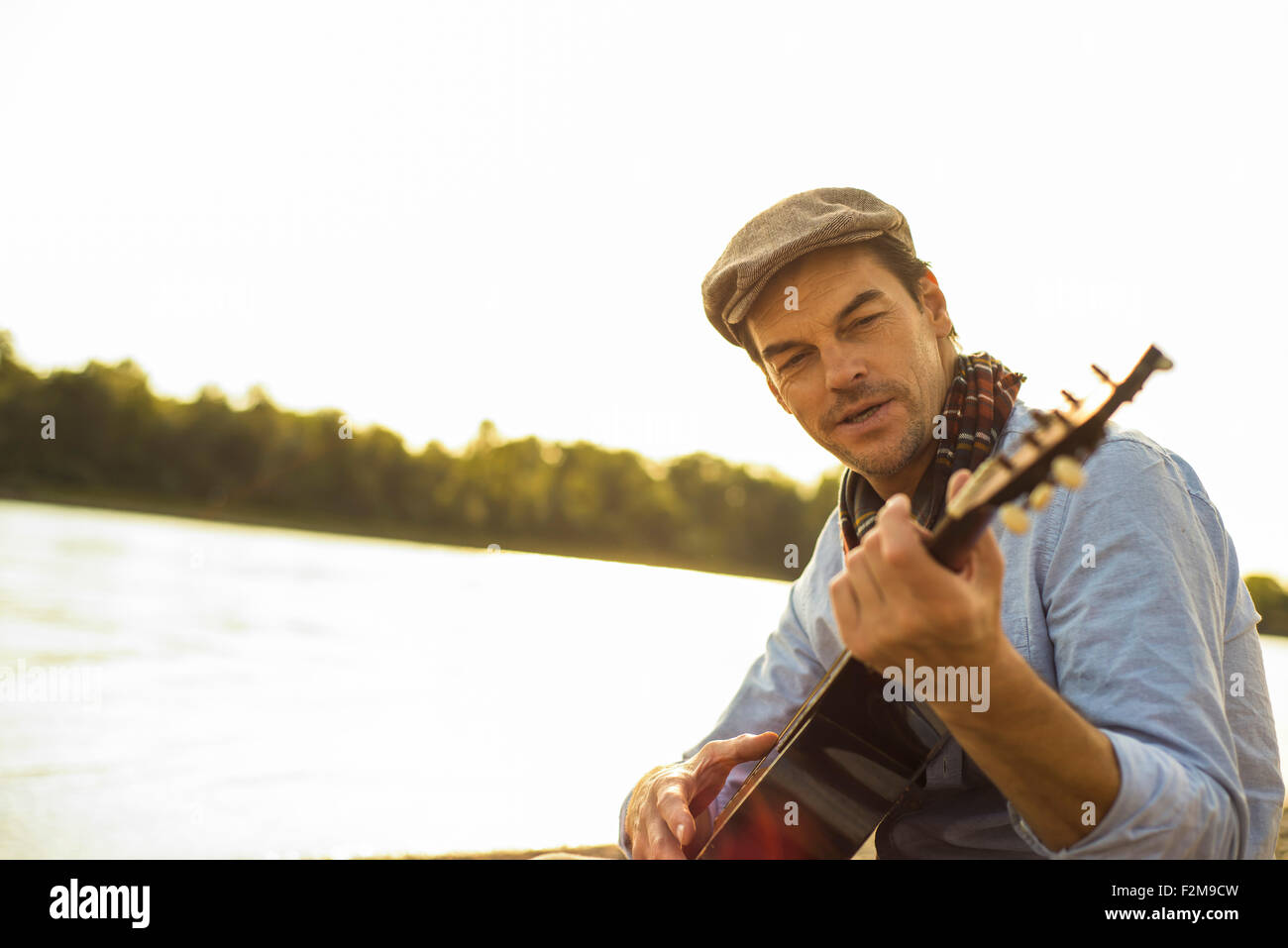Portrait of man playing guitar at riverside in the evening Stock Photo