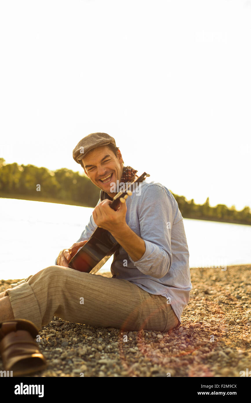 Portrait of happy man playing guitar at riverside in the evening Stock Photo