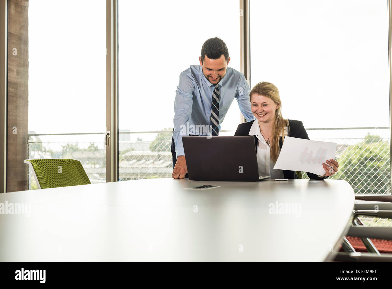 Smiling young businessman and businesswoman in conference room with laptop Stock Photo
