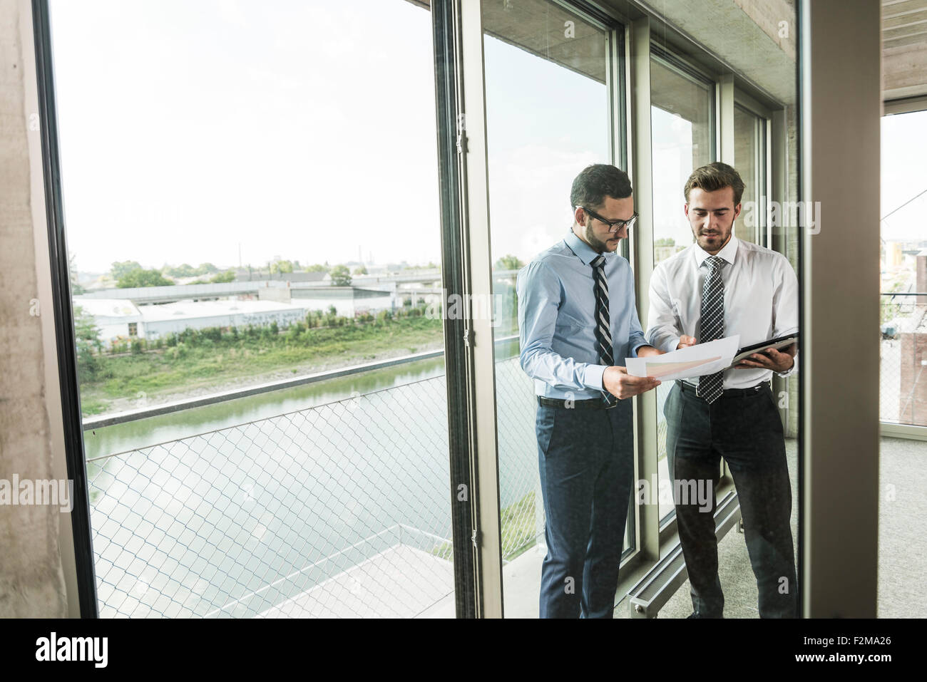 Two young businessmen discussing documents at the window Stock Photo ...