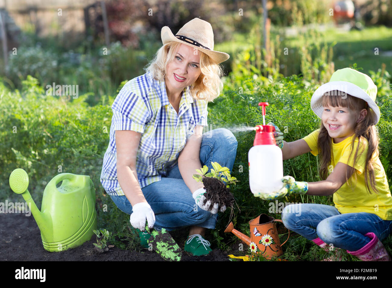 Happy woman and kid girl on farm garden in summer, planting strawberries. Happy family spending time together. Child helping mother. Stock Photo