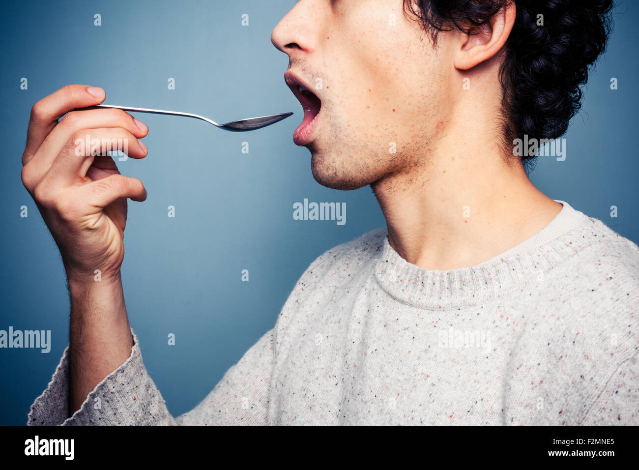Young man putting spoon in his mouth Stock Photo Alamy