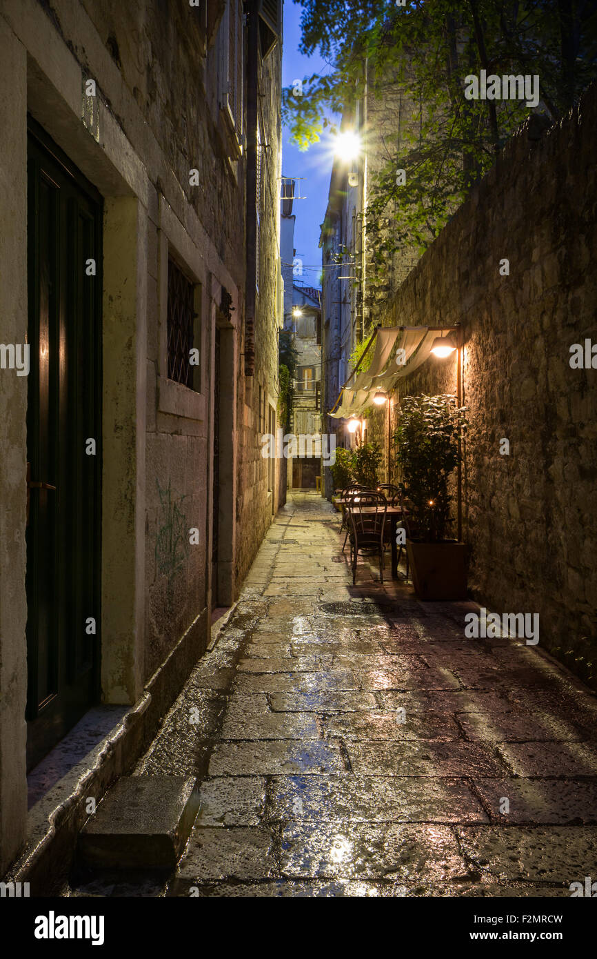 Narrow and empty alley with few cafe tables at the old town in Split, Croatia, at dark after rain. Stock Photo