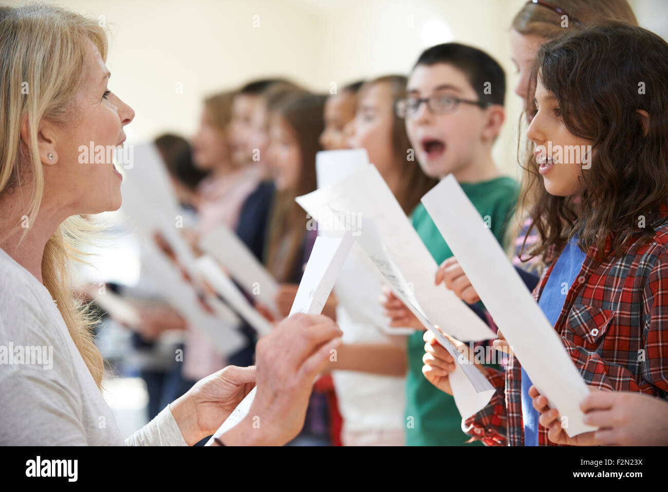 Children In Singing Group Being Encouraged By Teacher Stock Photo