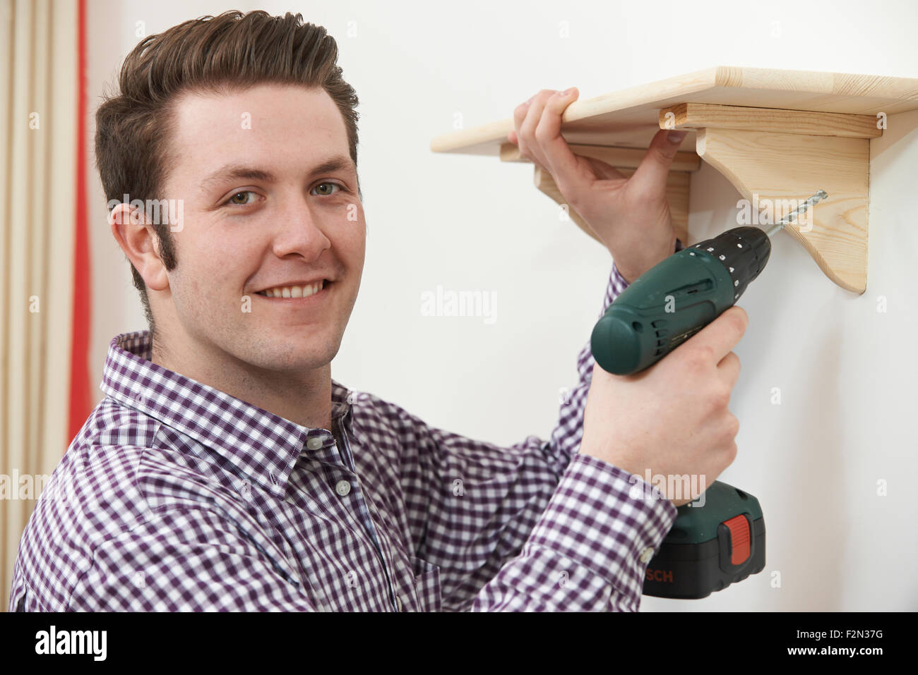 Man Putting Up Wooden Shelf At Home Using Electric Drill Stock Photo