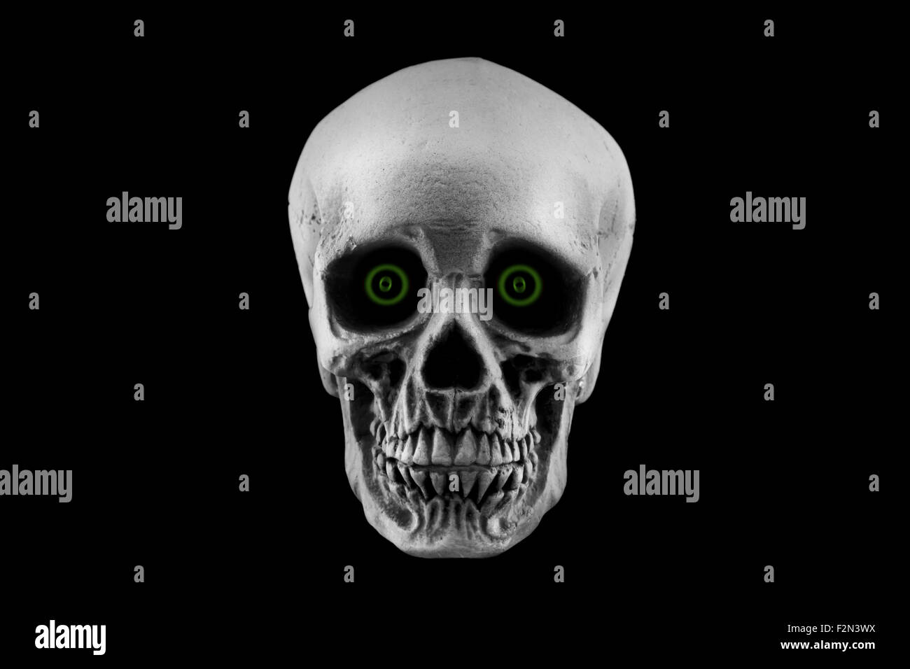 A Halloween skull decoration with green eyes isolated on a black background Stock Photo