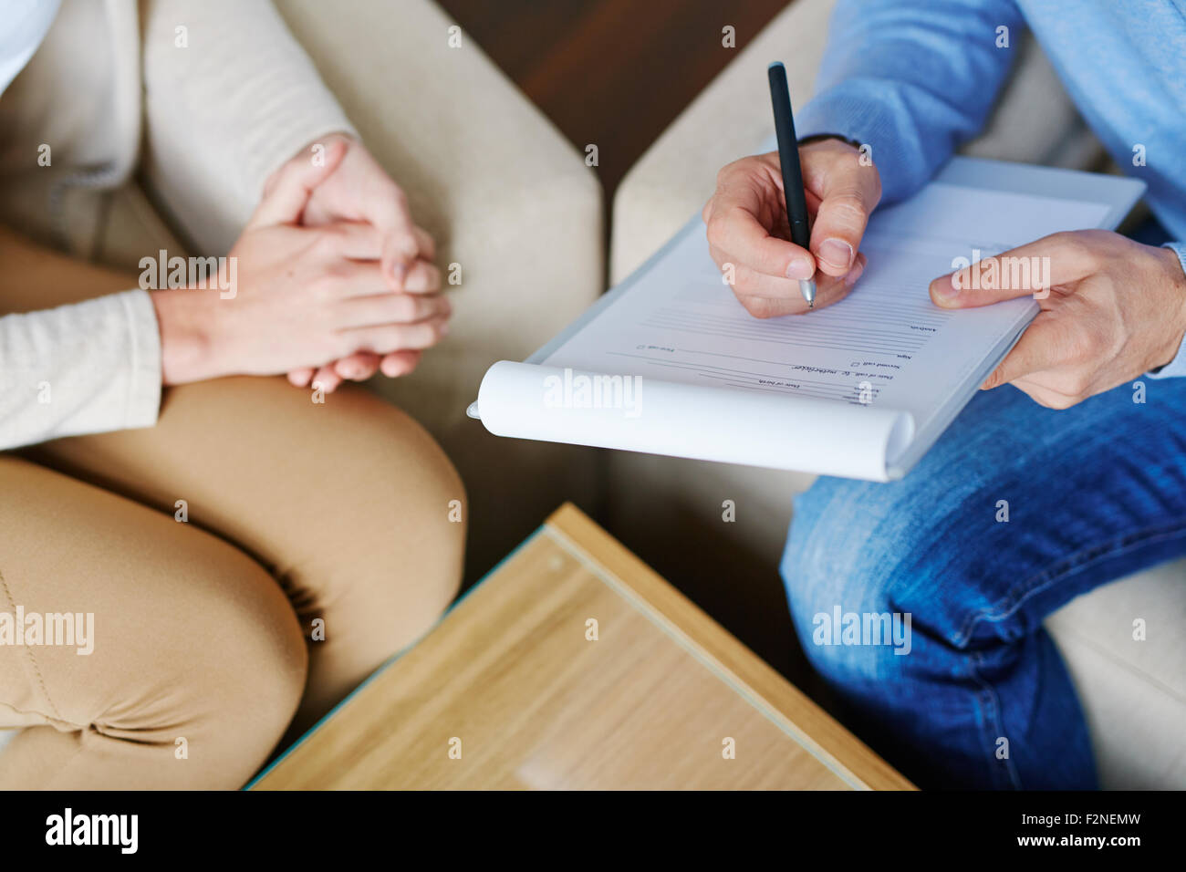 Hands of psychiatrist filling in medical document with patient near by