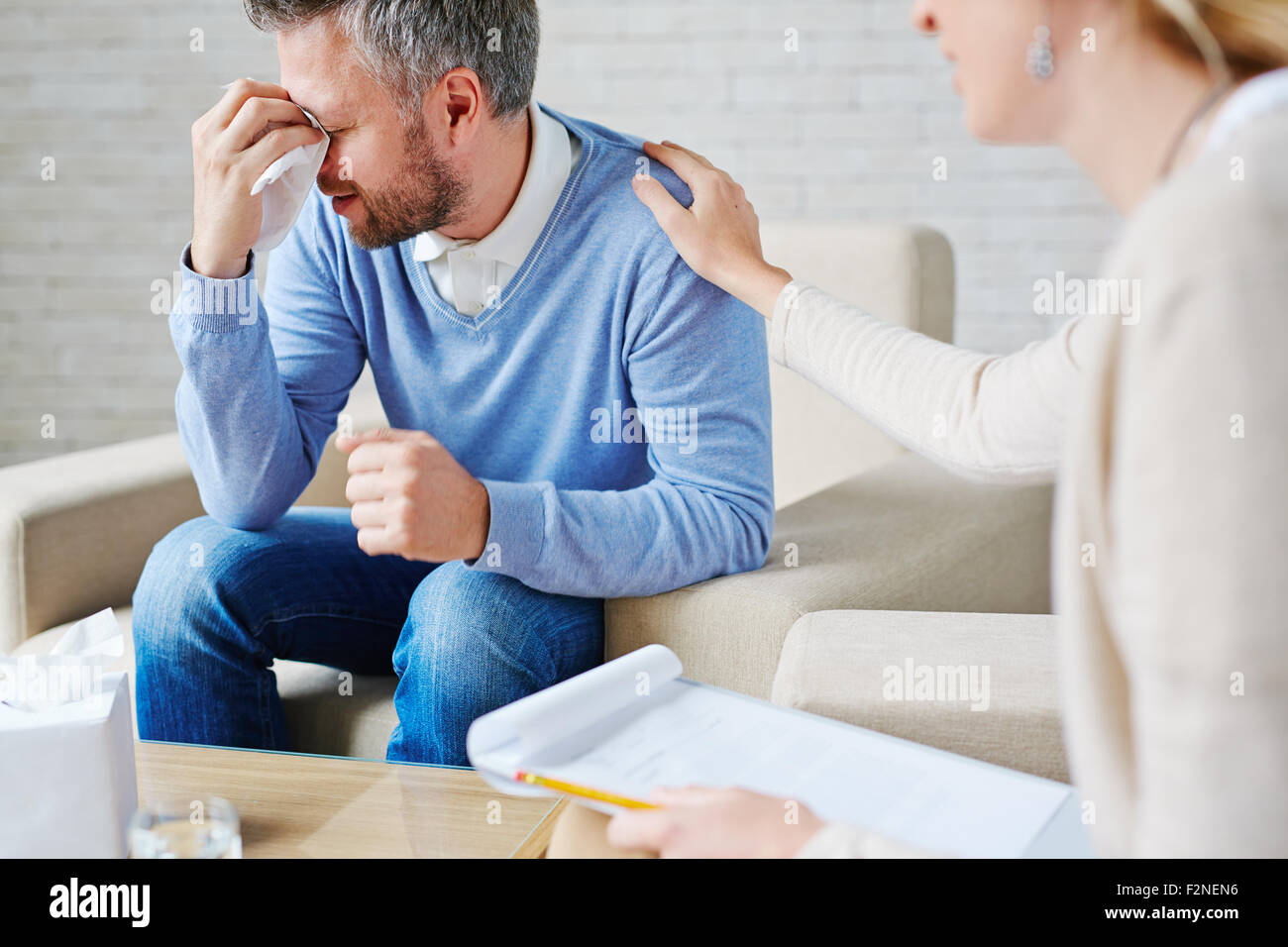 Crying man with handkerchief sitting by his psychologist Stock Photo