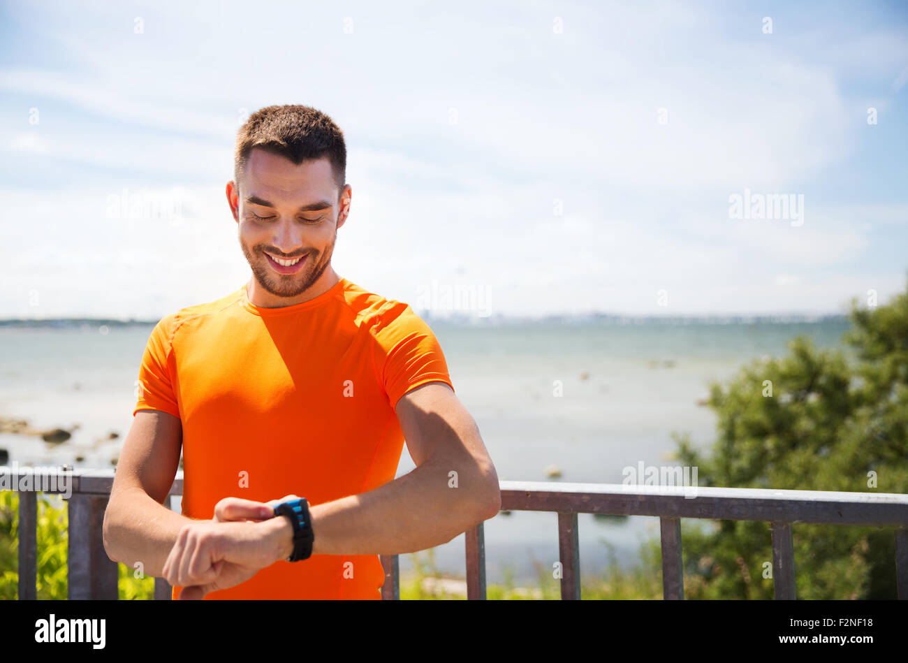 smiling young man with smart wristwatch at seaside Stock Photo