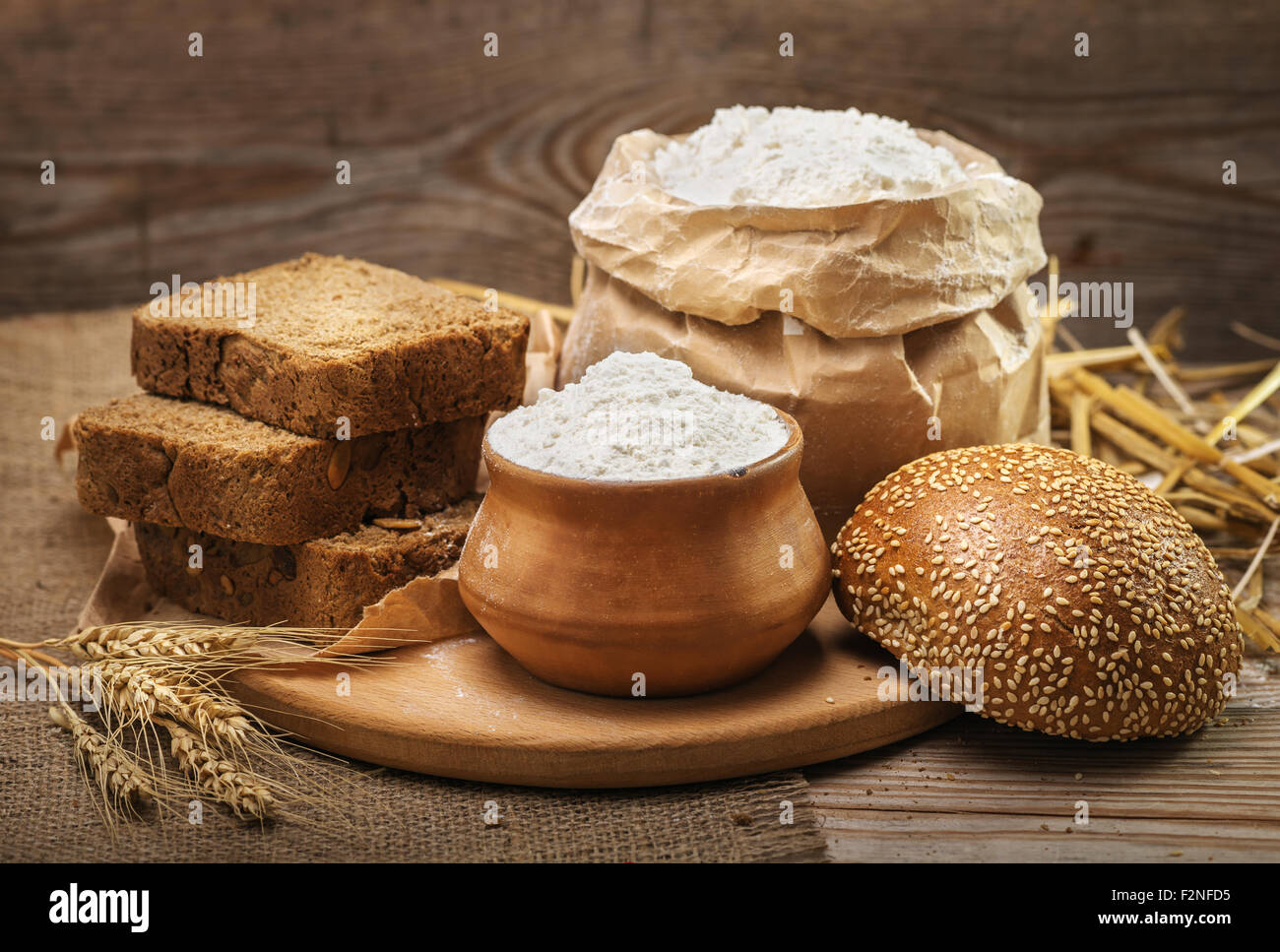 Wheat flour, sliced bread, bun with sesame seeds, wheat ears and straw on an old wooden background Stock Photo