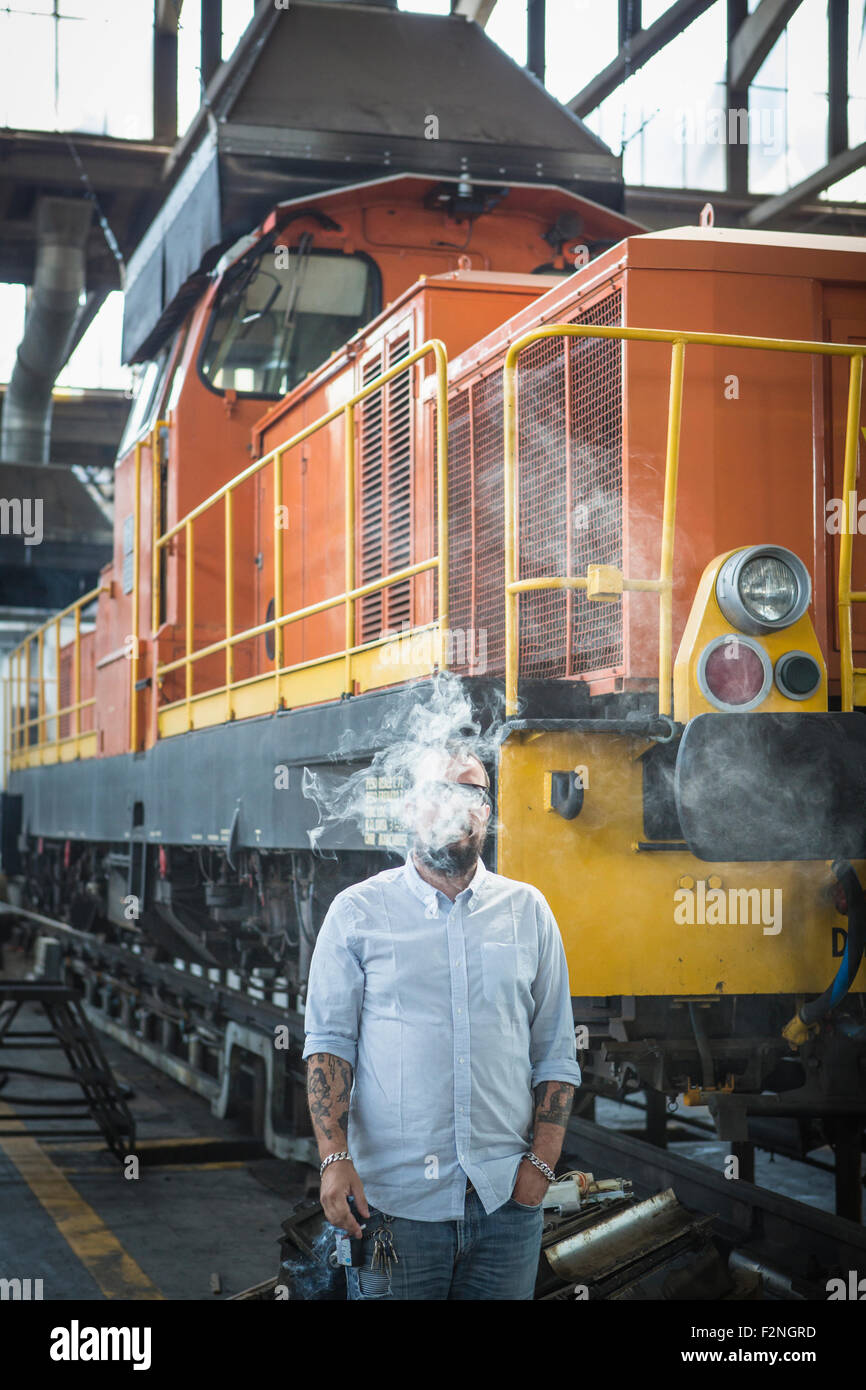 Caucasian man blowing smoke in train yard Stock Photo