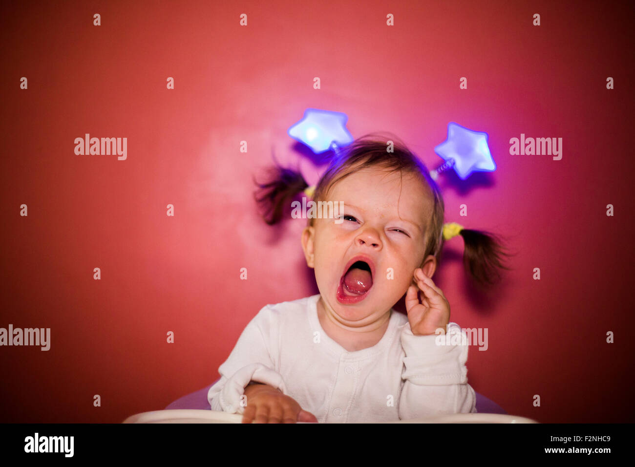 Caucasian baby girl wearing headband with stars and yawning Stock Photo