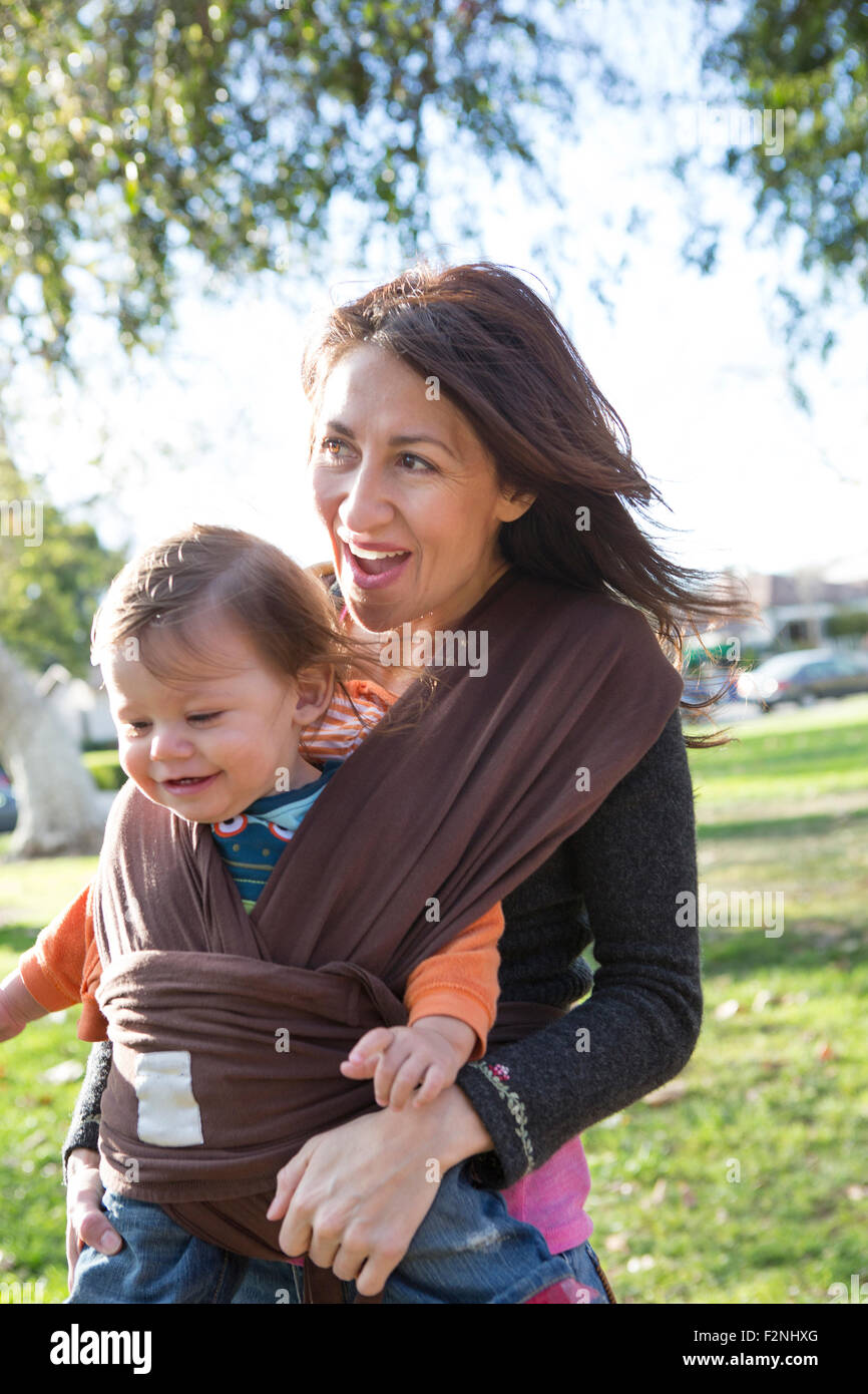 Hispanic mother wearing son in carrier in park Stock Photo