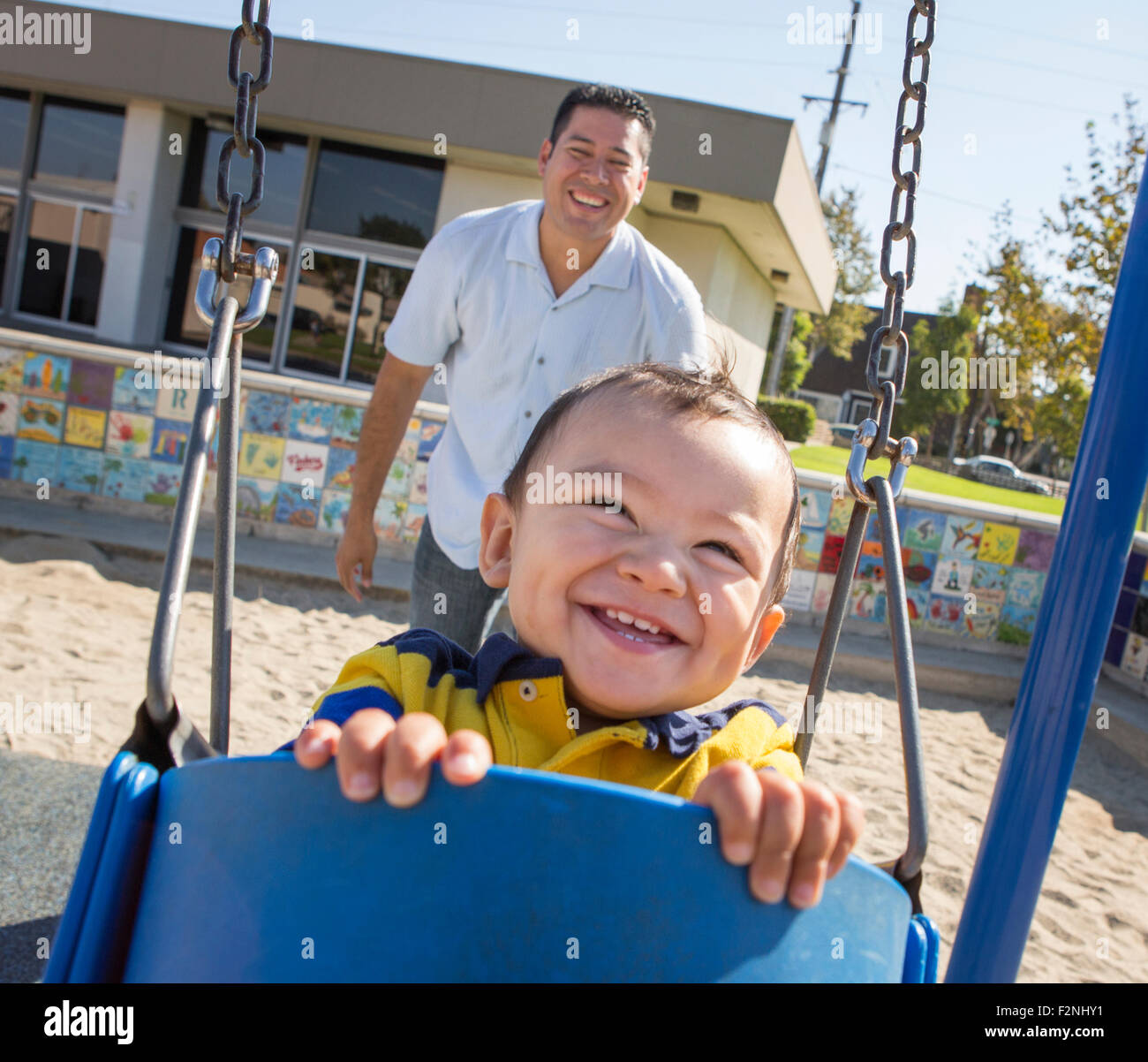 Hispanic father pushing son on playground swings Stock Photo