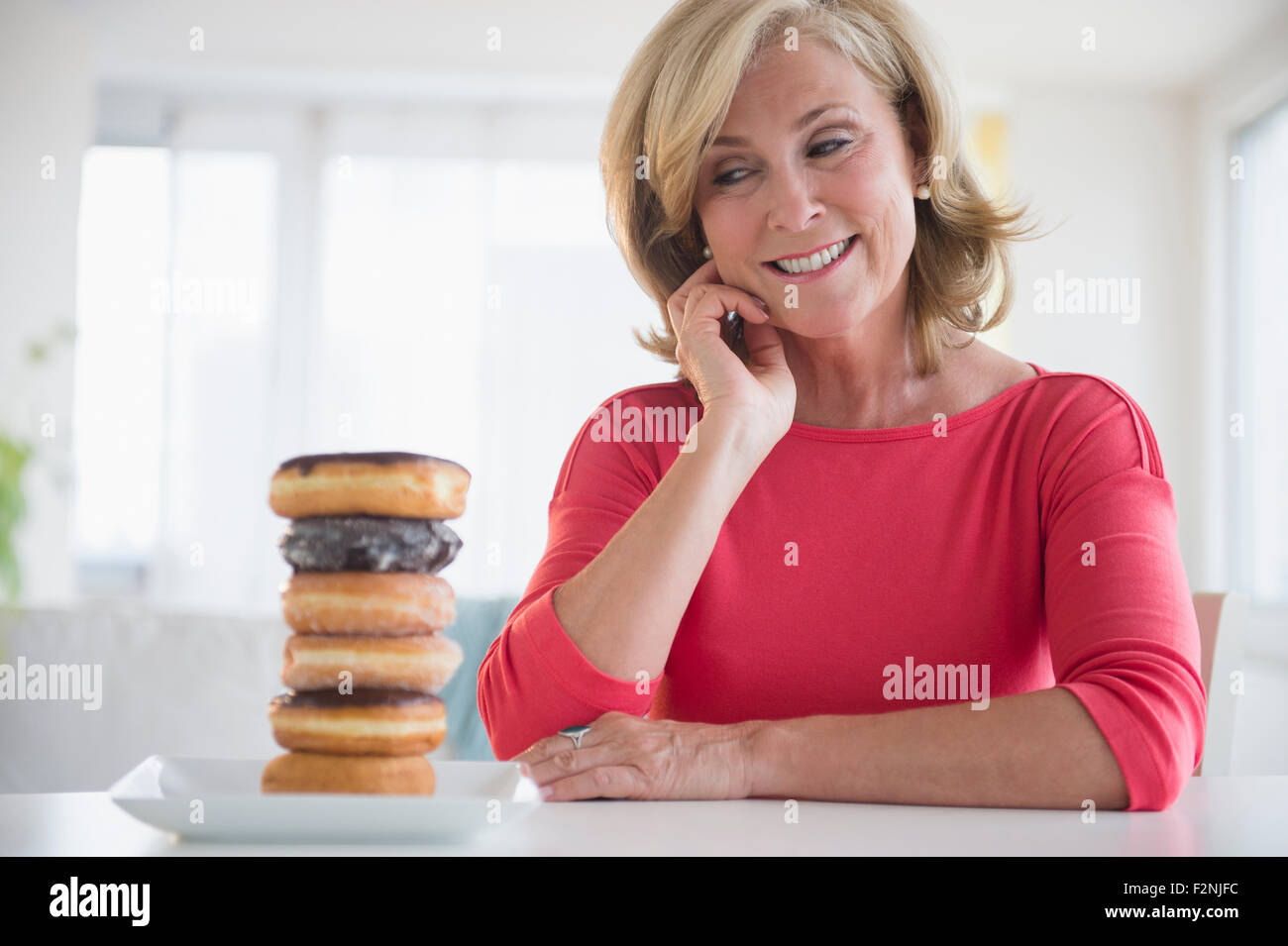 Caucasian woman admiring stack of donuts on table Stock Photo