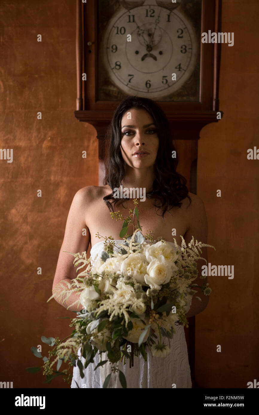 Bride holding bouquet of flowers under grandfather clock Stock Photo