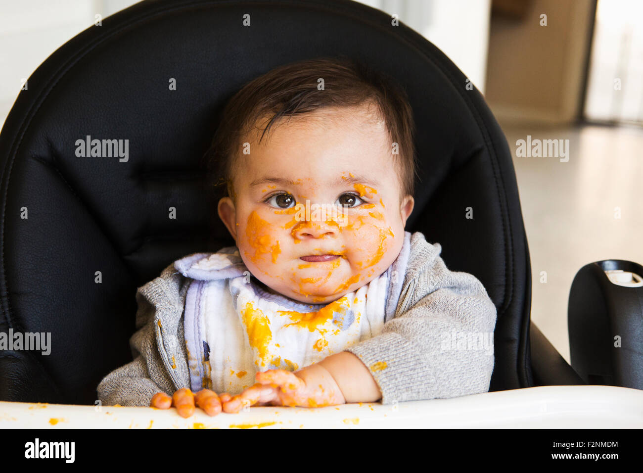 Messy Mixed race baby eating food in high chair Stock Photo