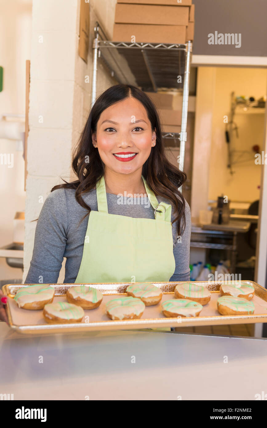 Asian baker holding tray of donuts in bakery Stock Photo Alamy