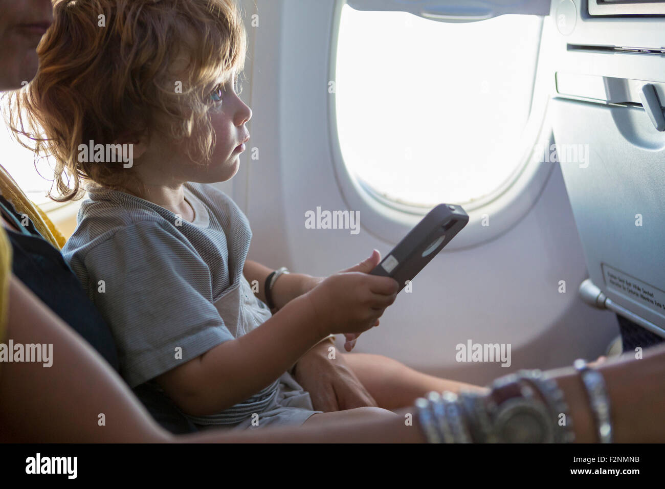 Caucasian mother and baby son using cell phone on airplane Stock Photo