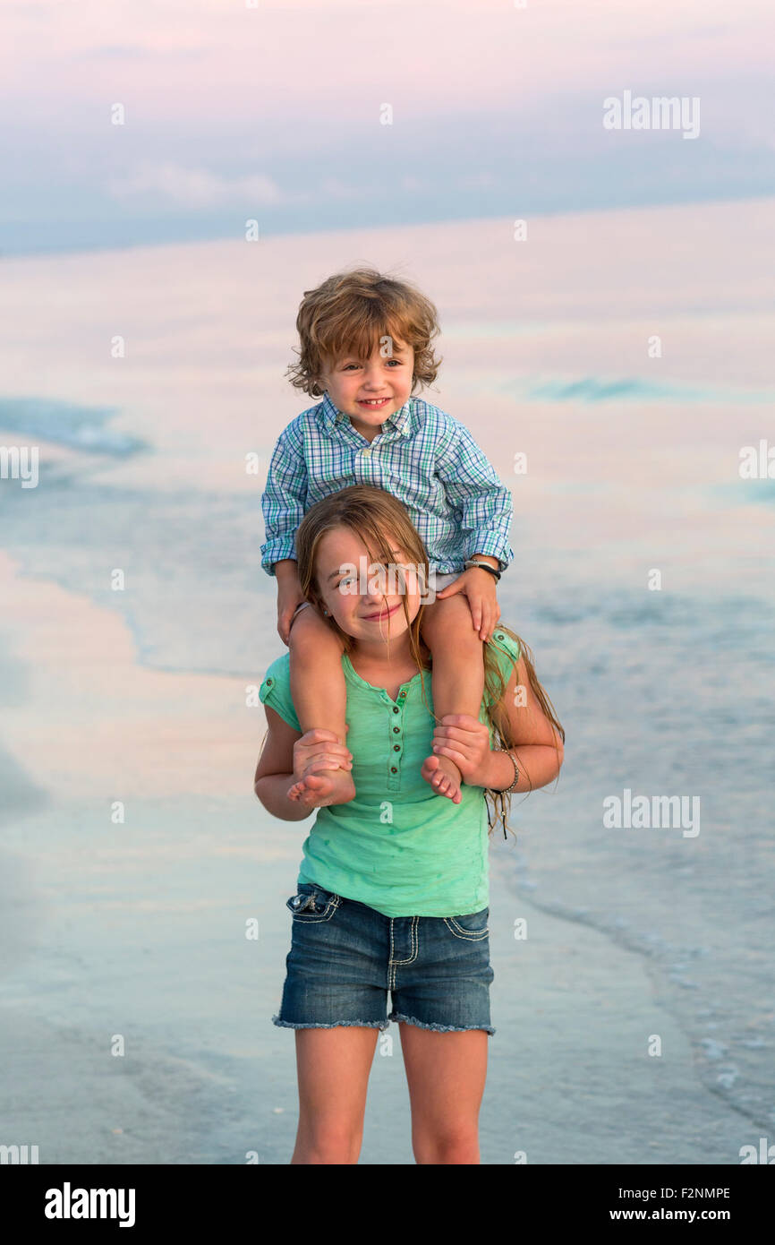 Caucasian girl carrying brother on shoulders on beach Stock Photo