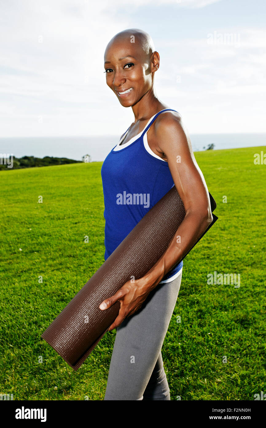 African American woman carrying yoga mat in park Stock Photo