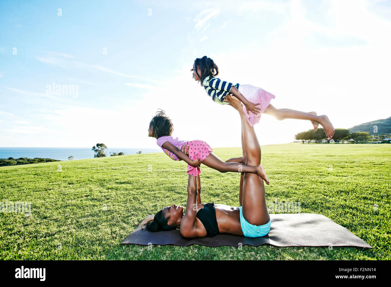 Mother holding children on yoga mat in park Stock Photo